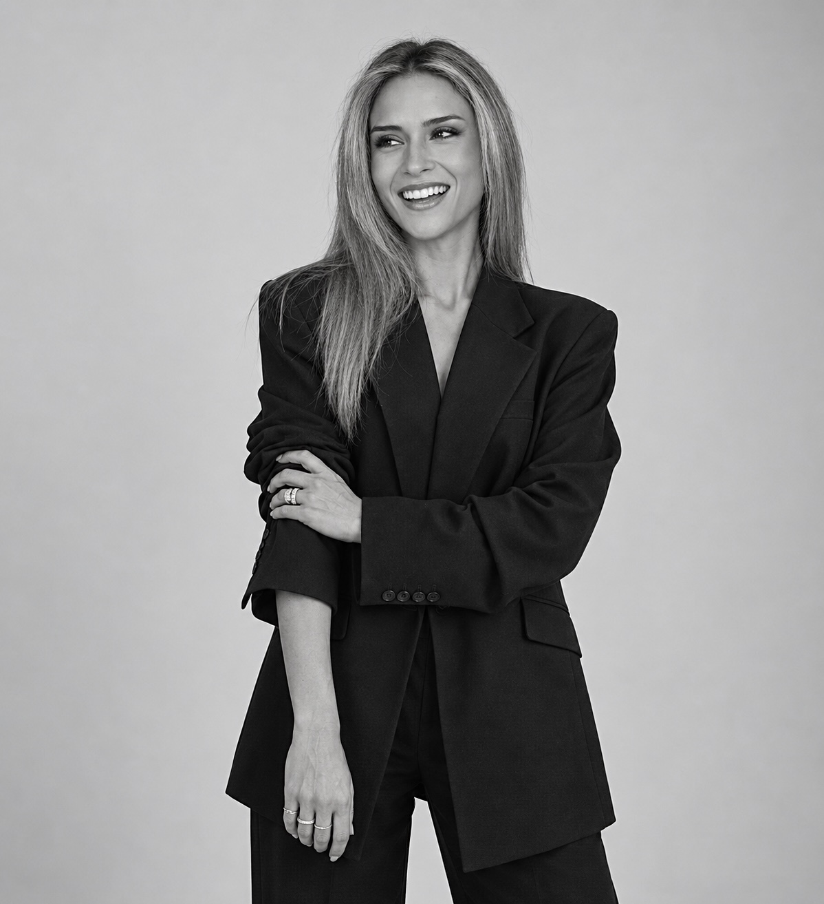 Ambar smiling in a black suit, photographed in black and white.